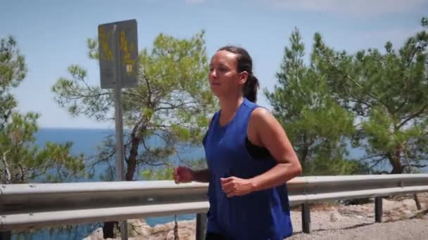 Portrait de souriante femme heureuse courant en plein air sur la route le long du littoral — Video