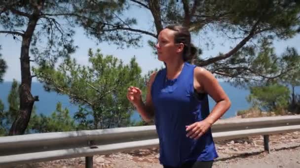 Активна усміхнена жінка біжить у лісі вздовж берега моря.Жінка займається спортом на відкритому повітрі — стокове відео