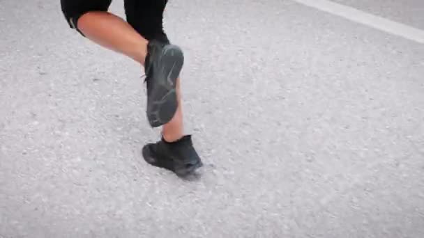Female legs in black sneakers running on empty asphalt road. Fitness activity — стоковое видео