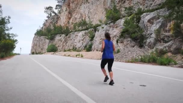 Uma mulher a correr ao ar livre. Jovem mulher ativa enérgica correndo na estrada da montanha — Vídeo de Stock