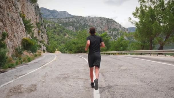 Man running outdoors. Male athlete jogging on road in mountains at sunny day — Stock videók