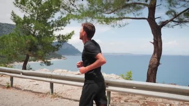 Young man running along rocky coastline. Athletic male training outdoors — Stockvideo