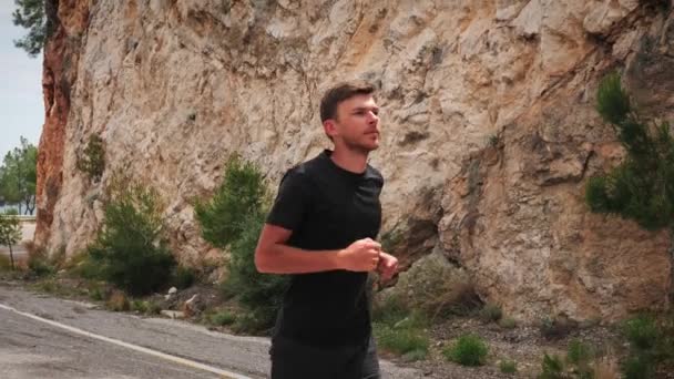 Corredor masculino jovem exercitando ao ar livre. Homem ativo correndo subida na estrada da montanha — Vídeo de Stock