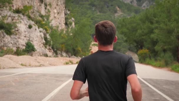 Corredor decidido corriendo en las montañas. Hombre practicando en carretera a lo largo de la costa — Vídeo de stock