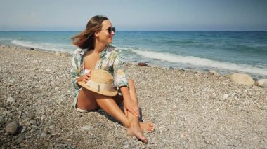 Genç ve neşeli kadın sahilde oturuyor ve yaz tatilinin tadını çıkarıyor.