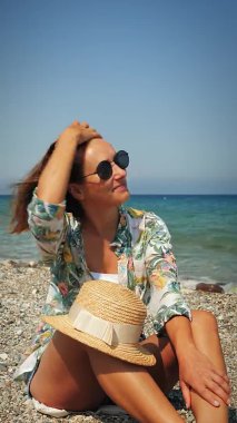 Rüzgarlı bir günde sahilde bir kadın. Gülümseyen kadın ufka bakıyor ve güneşin tadını çıkarıyor.