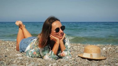 Plajda uzanan tropikal tişörtlü kahverengi saçlı çekici hippi kız.