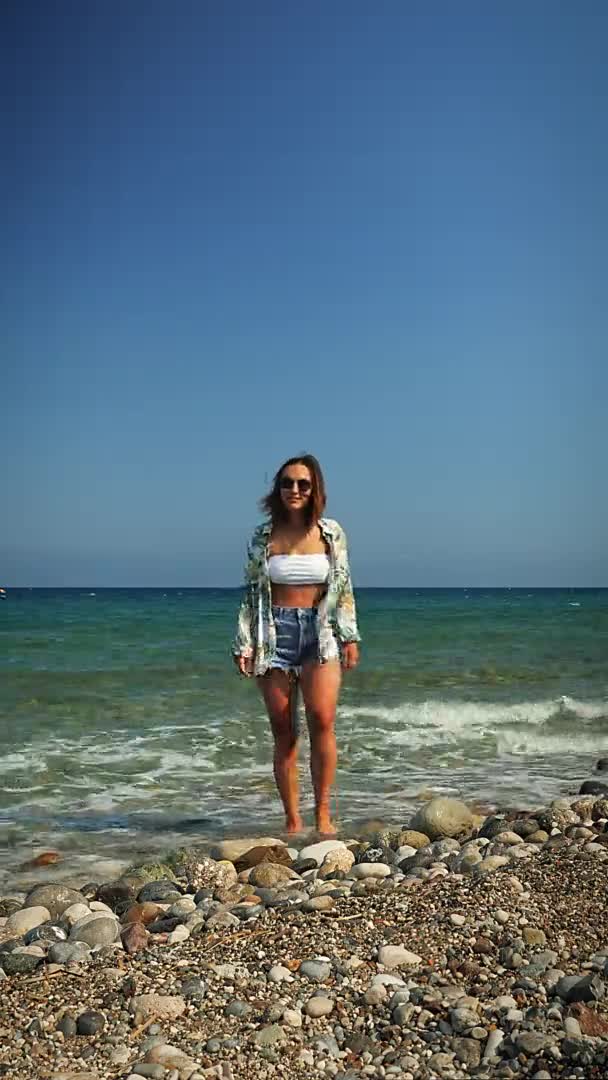 Carefree hipster surfer girl walking on pebble beach by the sea at windy day — Stock Video