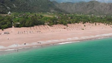 Geniş kumlu plajlı tropikal bir ada ve açık mavi deniz suyu.