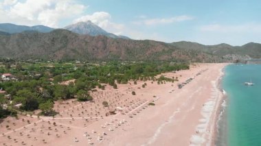 Sıcak yaz gününde sahili olan deniz kıyısı, arka planda yüksek dağ zirveleri