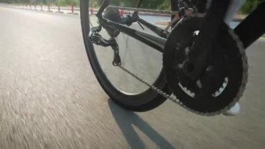 Bisiklet tekerleği sabah güneşinde dönüyor. Beyaz ayakkabılı erkek bacakları bisikletli pedalları çeviriyor. Gün batımında bisiklet yolunda bisiklet süren kaslı atletik bir adamın ayakları. Triatlon ve bisiklet konsepti