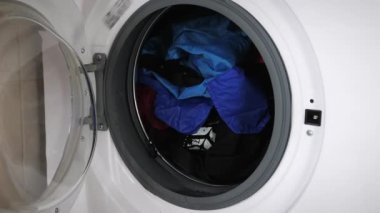 Kadın çamaşır makinesinin kapısını kirli çamaşırlarla kapatıyor, kapatın. Kadın evde temizlik yapıyor. Çamaşır makinesiyle çamaşır yıkayan bir kadın.