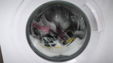 Modern çamaşır makinesi çamaşırları beyaz sabun köpüğüyle yıkıyor. Çamaşır makinesi rengarenk çamaşırlarla dolu. Dönen davul çamaşır makinesi, kapat