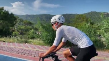 Bisiklet konsepti. Güneşli yaz gününde bisiklete binen adam. Beyaz kasklı ve beyaz bisiklet formalı şık erkek bisikletçi yarış sporu bisikletinde bisiklet sürüyor, yoğun kardiyo çalışması yapıyor. Spor motivasyonu