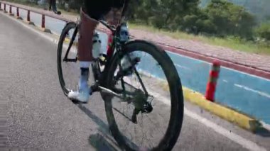 Beyaz bisiklet ayakkabıları ve çoraplar içinde ince, kaslı erkek bacakları spor yol bisikletinde pedalları büker. Yaklaş. Bisiklet tekerleği ve sürüş sistemi dönüyor. Bisiklet kasetini ve zincir dönüşünü kapat