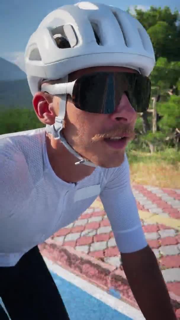 自転車に乗っている間に自撮りしている男 垂直ビデオ ヘルメットの若い男性選手や自転車でサングラスサイクリングやスマートフォン上でセルフィービデオを作る サイクリングとトライアスロンのコンセプト — ストック動画