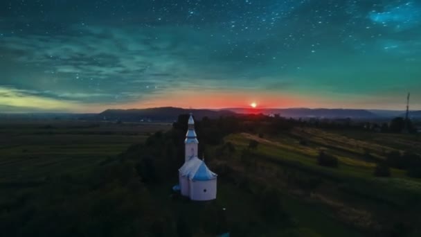 教会と自然の風景の上に夕日と雲の空中高波 背景に山の丘のあるフィールドでの夏の夕日 — ストック動画