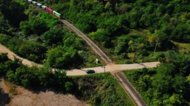 Renkli yük vagonları olan bir yük lokomotifi demiryolu demiryolu ile kırsal otoyolda ilerliyor. Yük treni yeşil ormandan ve kırsal yoldan geçiyor. Ulaşım kargo teslimatı