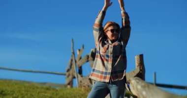 Yeşil dağ çayırındaki güzel sarışın kadın açık mavi gökyüzüne karşı. Sıcak bir sonbahar gününde kırsal bölgeleri ve kır çiçeklerini keşfeden gündelik giysiler içindeki genç bir kadın. Seyahat hedefi kavramı