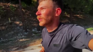 Man selfie while running at sunny summer day. Portrait of perspiring active male runner running outdoors in mountains and making selfies. Handsome male athlete jogging in green forest. Sport activity