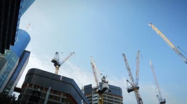 Yellow construction cranes above skyscrapers. Construction of skyscrapers over blue sky. Construction of high-rise office business buildings at daytime against blue sky with clouds