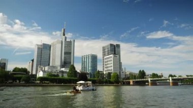 Gökdelenler bulutlu gökyüzüne karşı. Kabarık bulutlu gökyüzü altında gökdelenler, zaman ayarlı. Güneşli bir günde nehir kıyısındaki yüksek katlı ofis binası. Gökdelenler ufukta hızla hareket eden bulutlar