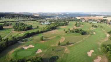 Golf sahasında uçuyor. Yeşil çimenli ve küçük gölü olan golf sahaları. Kırsal bölgedeki yeşil tepelerin hava manzarası. Güneşli yaz gününde göllü ve ağaçlı golf sopası.