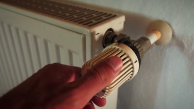 Hand adjusting temperature of radiator. Man turns regulator knob in radiator thermostat