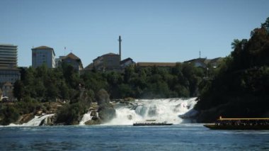 Huge massive waterfall on Rhine river in Switzerland. Rhine Falls with power water stream and tourist ships floating near waterfall. Travel destination and tourism concept. Amazing nature landscape