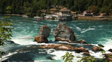 Red flag of Switzerland waving in wind at Rhine waterfall. Huge massive waterfall on Rein river at sunny summer day. Popular travel destinations and tourism concept
