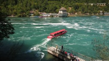 Red tourist boat with tourists floating on Rhine river in Schaffhausen, Switzerland. Small red ship with flag of Switzerland with people floating near Rhine waterfall. Popular travel destinations