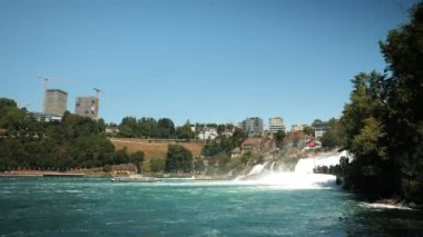 Waterfall on Rhine river in Switzerland. Huge massive water power stream of Rhine river with tourists boats floating near waterfall. Popular travel destinations and tourism concept