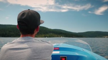 Back view of man controlling and driving electric boat ship. Male floating on tourist ship along mountain lake. Holiday vacation and weekend concept. Sailing regatta. Professional yachtsman