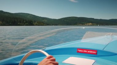 Male hands turning wheel on electric boat. Man driving sailing yacht along mountain lake surrounded by green trees. Man sailing on water, close up of boat wheel