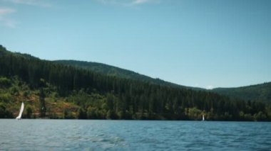 Sailing on lake. Floating on boat along mountain lake with green trees and hills at horizon. Summer vacation concept. Travel and tourism concept. Clear water of mountain lake