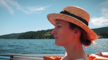 Portrait of cheerful charming woman in straw hat floating on boat, enjoying beautiful nature during summer vacation. Happy smiling female sailing on tourist ship, relaxing and resting at sunny day