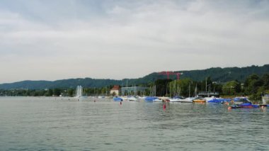 Zurich lake at cloudy summer day. Moored boats and yachts at marina with fountain at Zurich lake in Switzerland. Beautiful nature landscape with green hills and cottage houses against lake