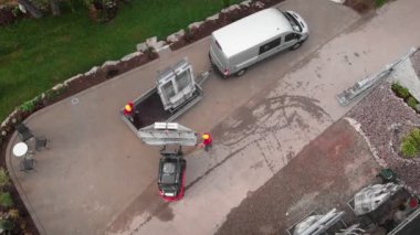 Workers in protective helmets loading PVC window frames in truck at construction site. Builders pulling white window frames with glass into vehicle machine. House under construction