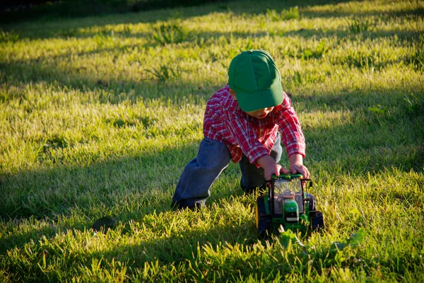 Ein junger Bauernjunge schiebt einen Spielzeugtraktor nach draußen — Stockfoto