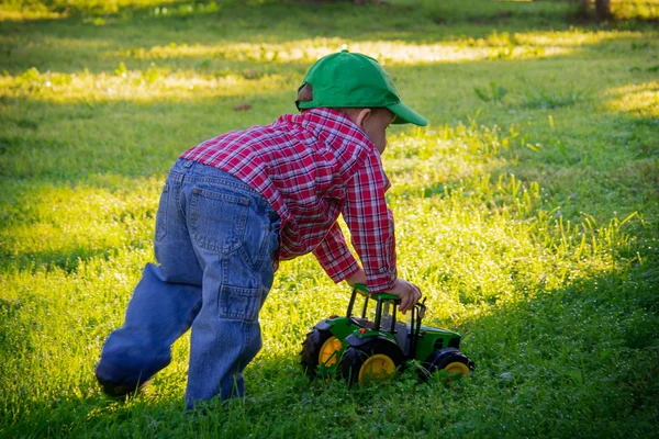 Un jeune garçon pousse un tracteur de jouet dans l'herbe Photos De Stock Libres De Droits