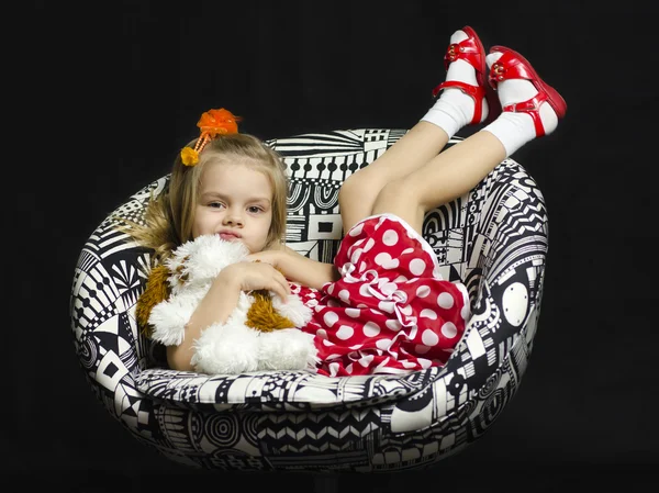 A little girl with a soft toy on a chair — Stock Photo, Image