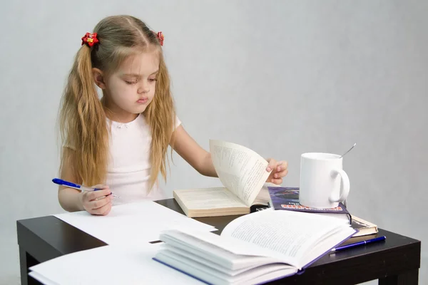 Meisje bladeren door het boek en schreef op een vel papier abstracte vergadering aan de tafel — Stockfoto