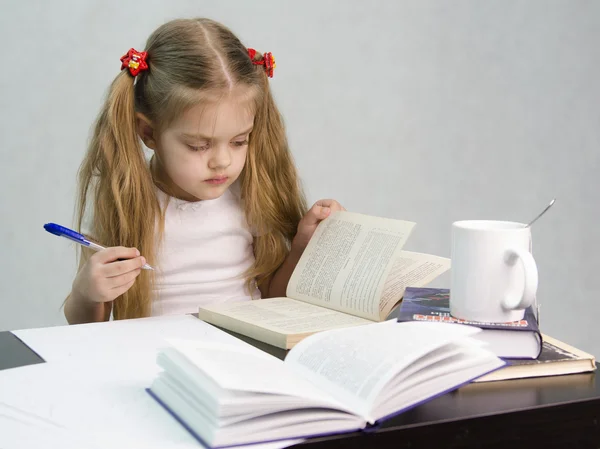 Menina folheando o livro e escreveu em uma folha de papel abstrato sentado à mesa — Fotografia de Stock