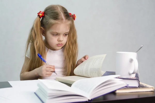 Meisje bladeren door het boek en schreef op een vel papier abstracte vergadering aan de tafel — Stockfoto