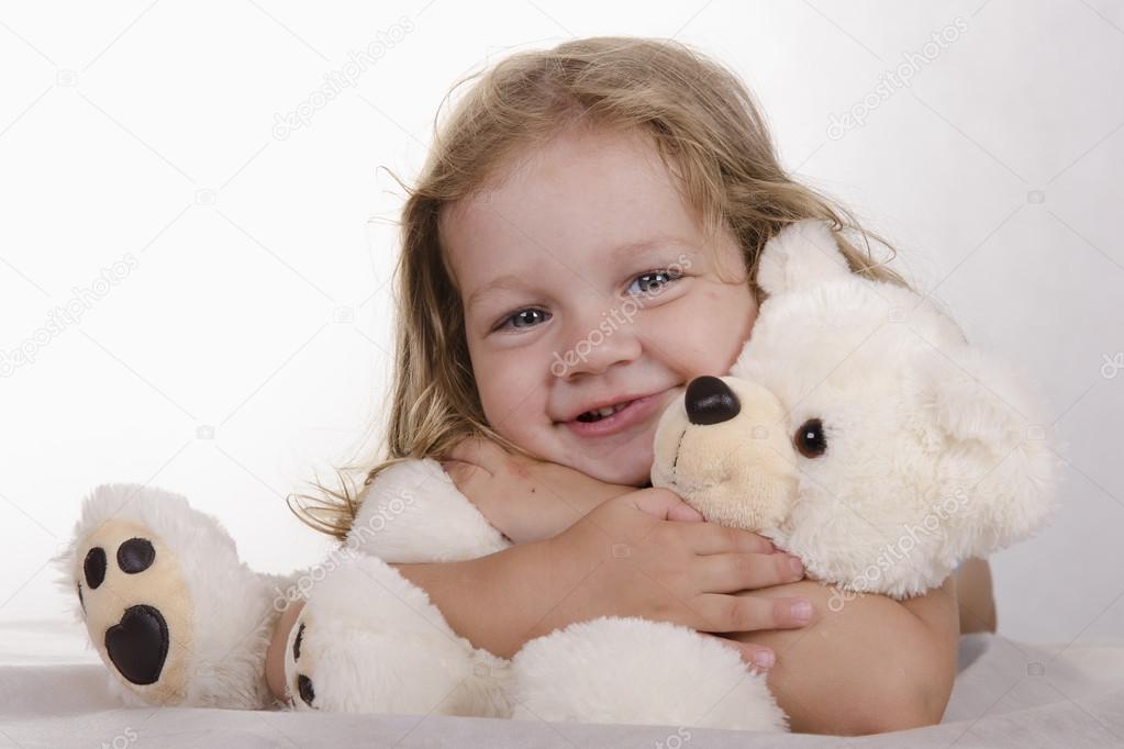 Two-year-old girl lies and bear hugs