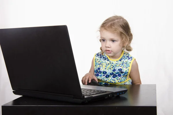 Het meisje dat zit aan de tafel en lopende laptop — Stockfoto