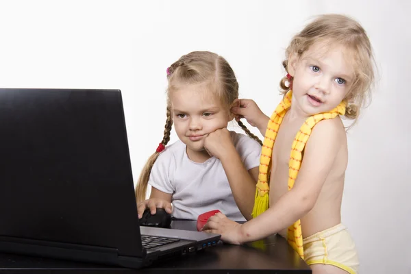 Dziewczyna pracuje na laptopie. inna dziewczyna podszedł do niej i wziął jedną z jej do ucha — Zdjęcie stockowe