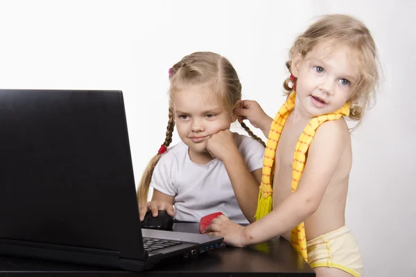 A rapariga que trabalha num portátil. Outra menina aproximou-se dela e pegou um de seus ouvidos — Fotografia de Stock