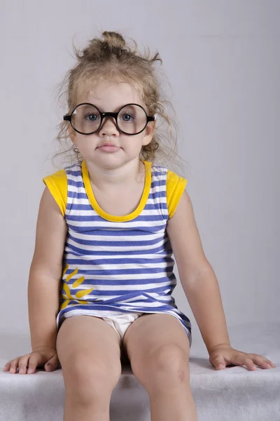 Two-year-old κορίτσι σε γυαλιά αστεία συνεδρίαση ψάχνει στο πλαίσιο. πορτρέτο — Φωτογραφία Αρχείου