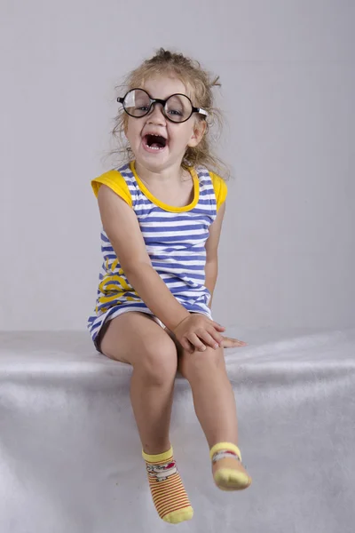 Two-year-old girl in funny glasses sits and laughs cheerfully — Stock Photo, Image